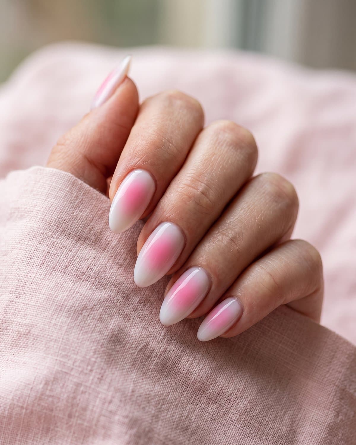 Almond aura nails with a milky white base and a soft hot pink airbrushed glow in the center of each nail, on pale pink linen