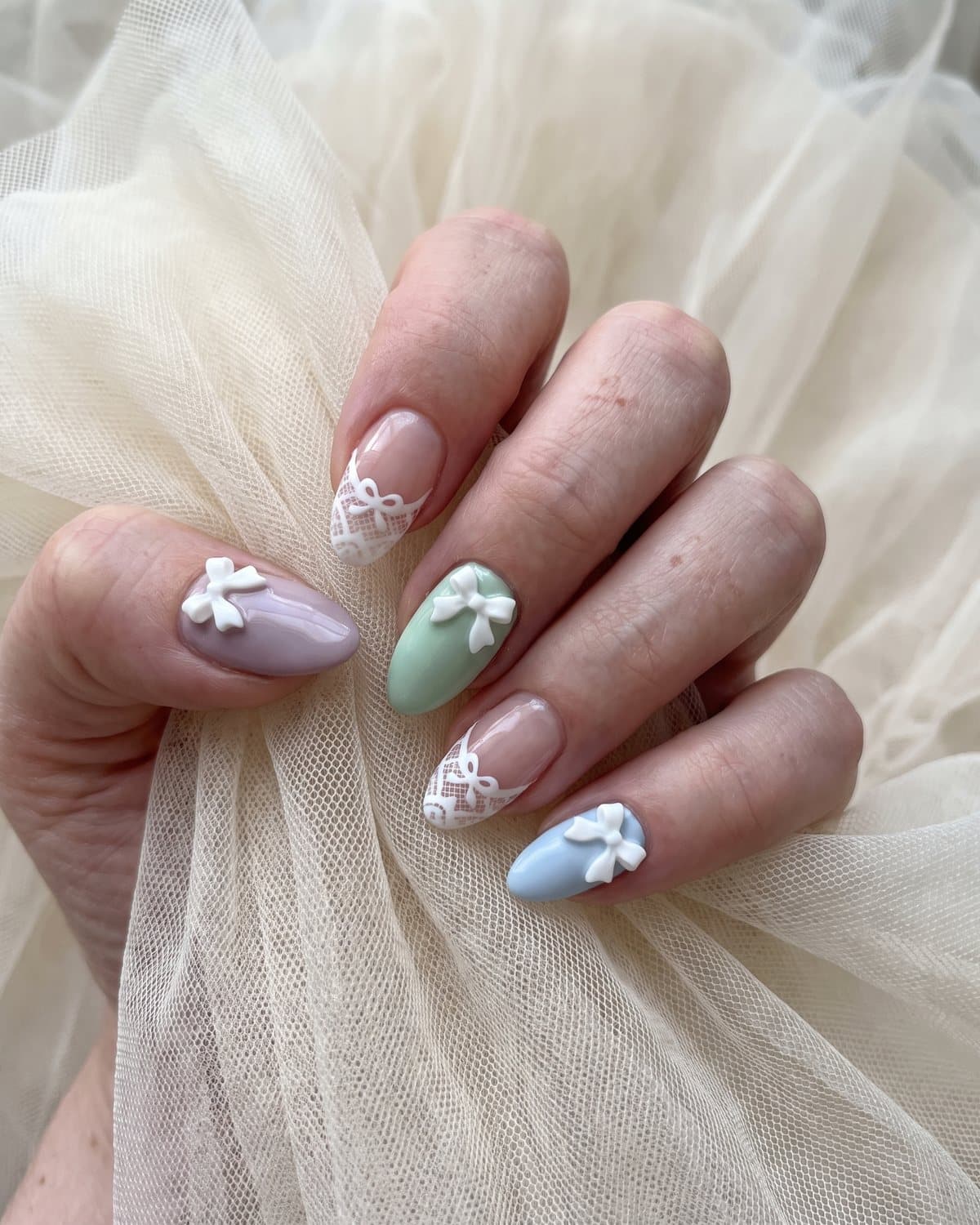 Almond nails with white lace pattern tips and tiny bows, and mismatched pastel nails in lilac, mint and baby blue each with a small white bow