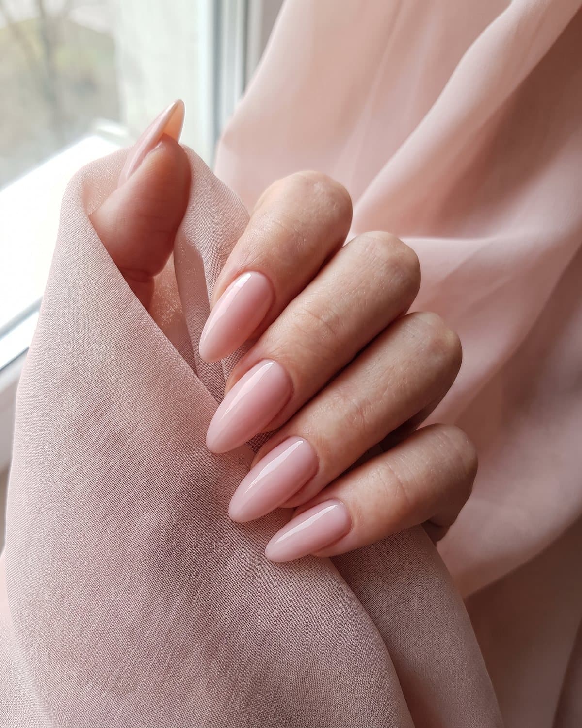Glossy almond nails in soft blush pink, resting on blush pink chiffon