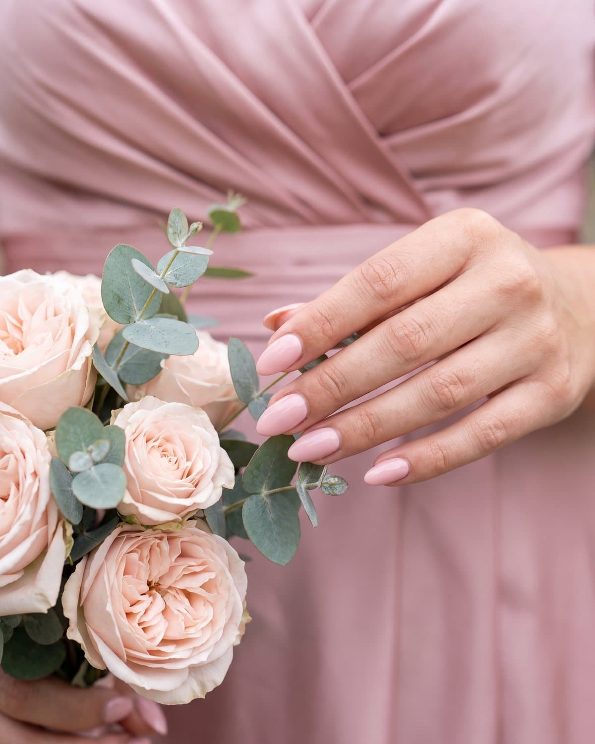 Bridesmaid holding a bouquet of blush roses and eucalyptus with glossy almond nails in soft blush pink