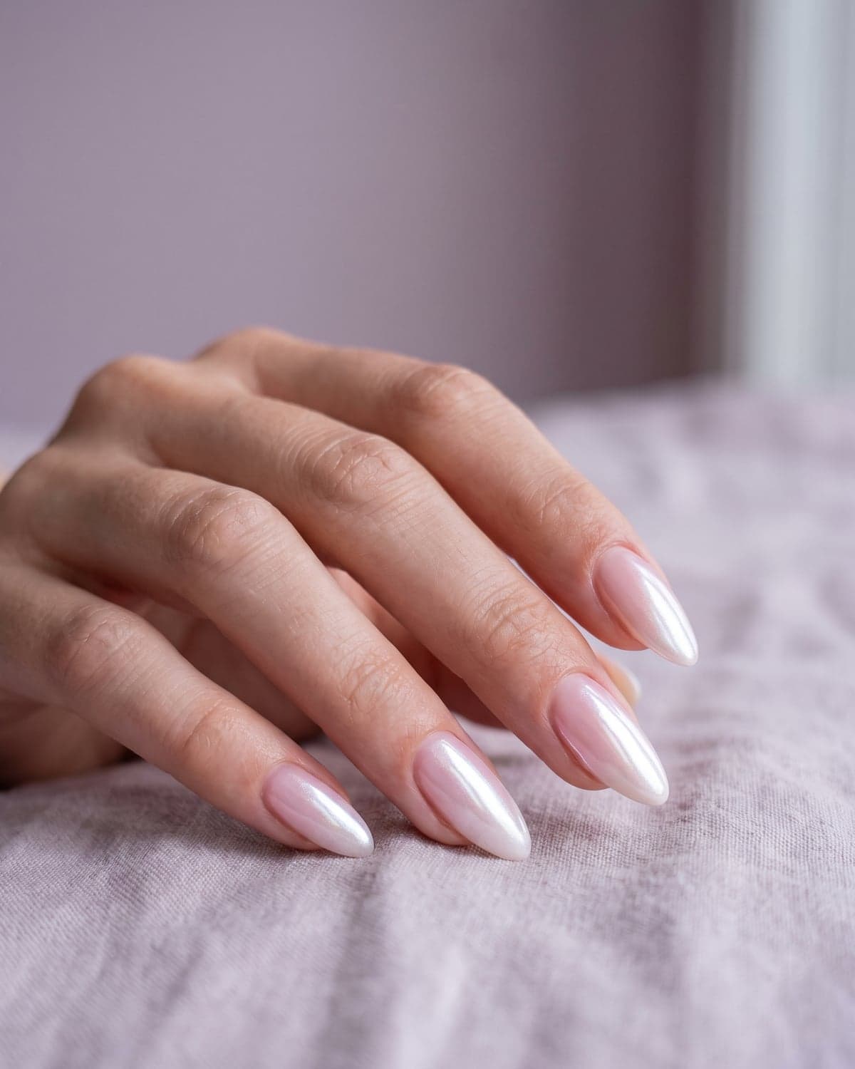 Glazed donut chrome almond nails with a pearly sheen on a soft lilac background