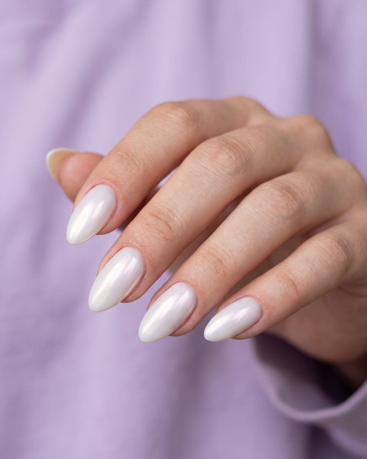 Glazed pearly chrome almond nails with a soft shimmer on a light lavender background