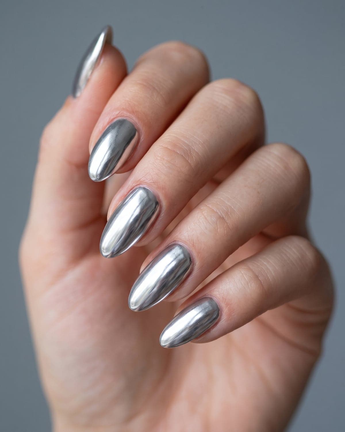Mirror silver chrome almond nails with a high-shine metallic finish on a cool gray background