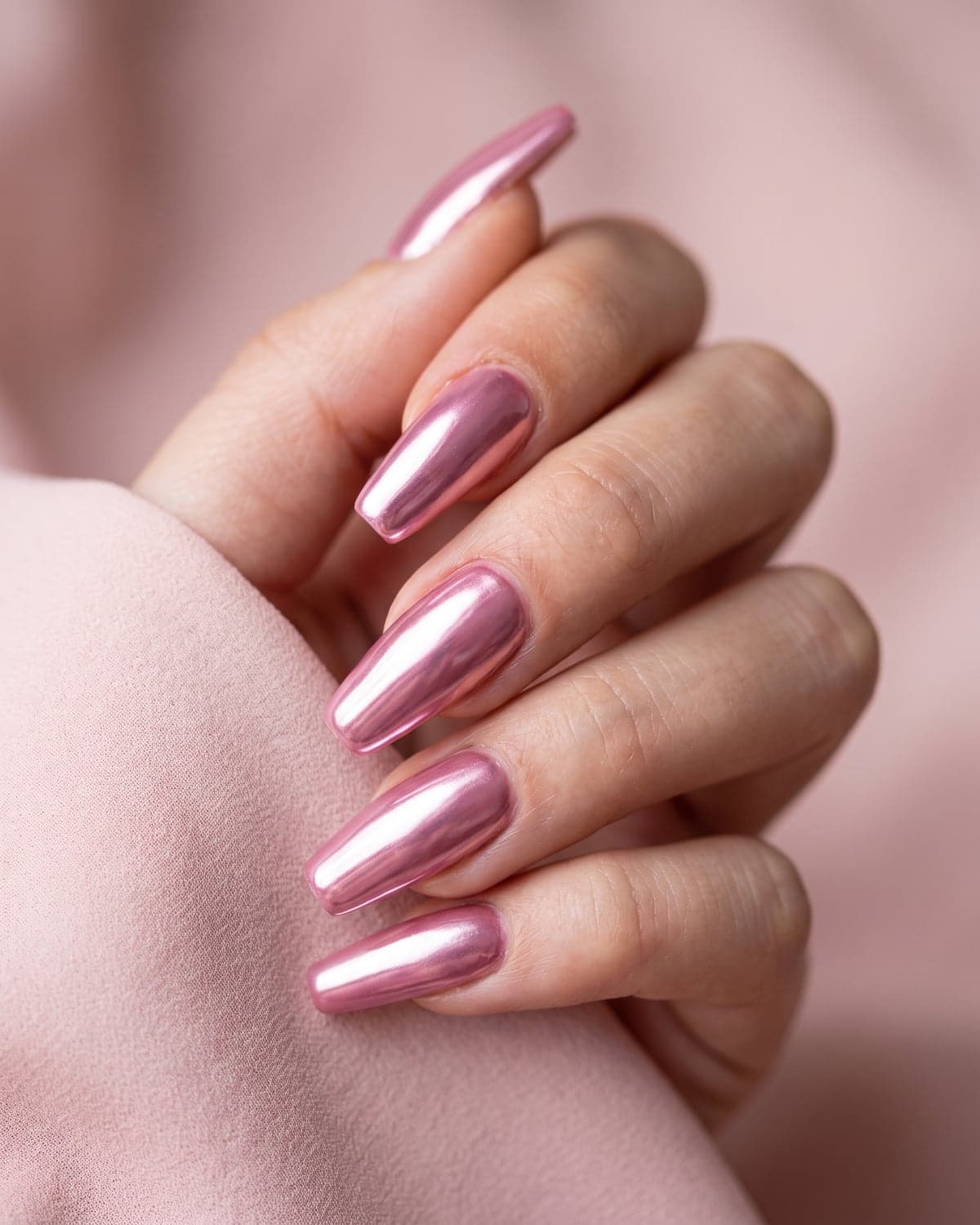 Pink chrome coffin nails with a high-shine metallic finish on a soft pink background