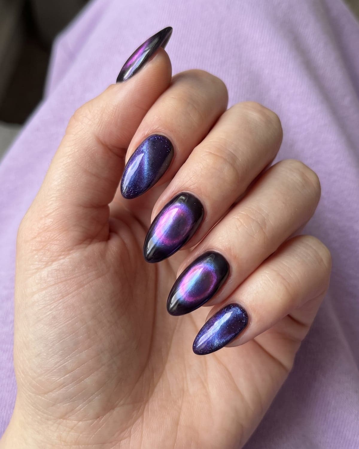 Aura chrome and cat-eye almond nails in purple and blue with glowing centers on a lilac background