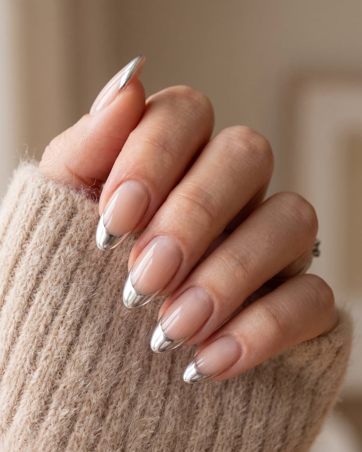Silver chrome French tip almond nails on a nude base with a soft neutral background