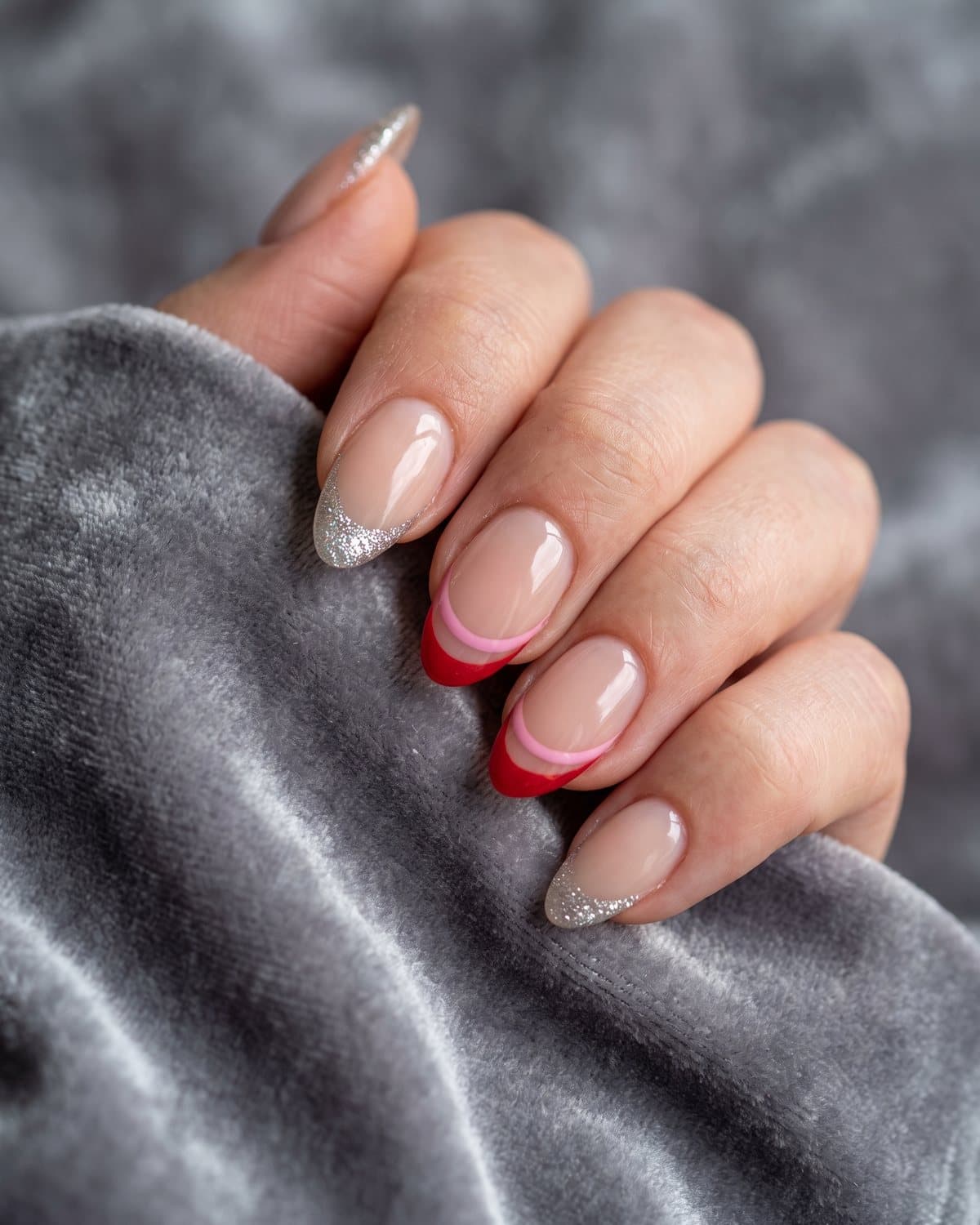 Almond nails with sparkly silver glitter French tips and two-tone pink and red double French tips, on grey velvet