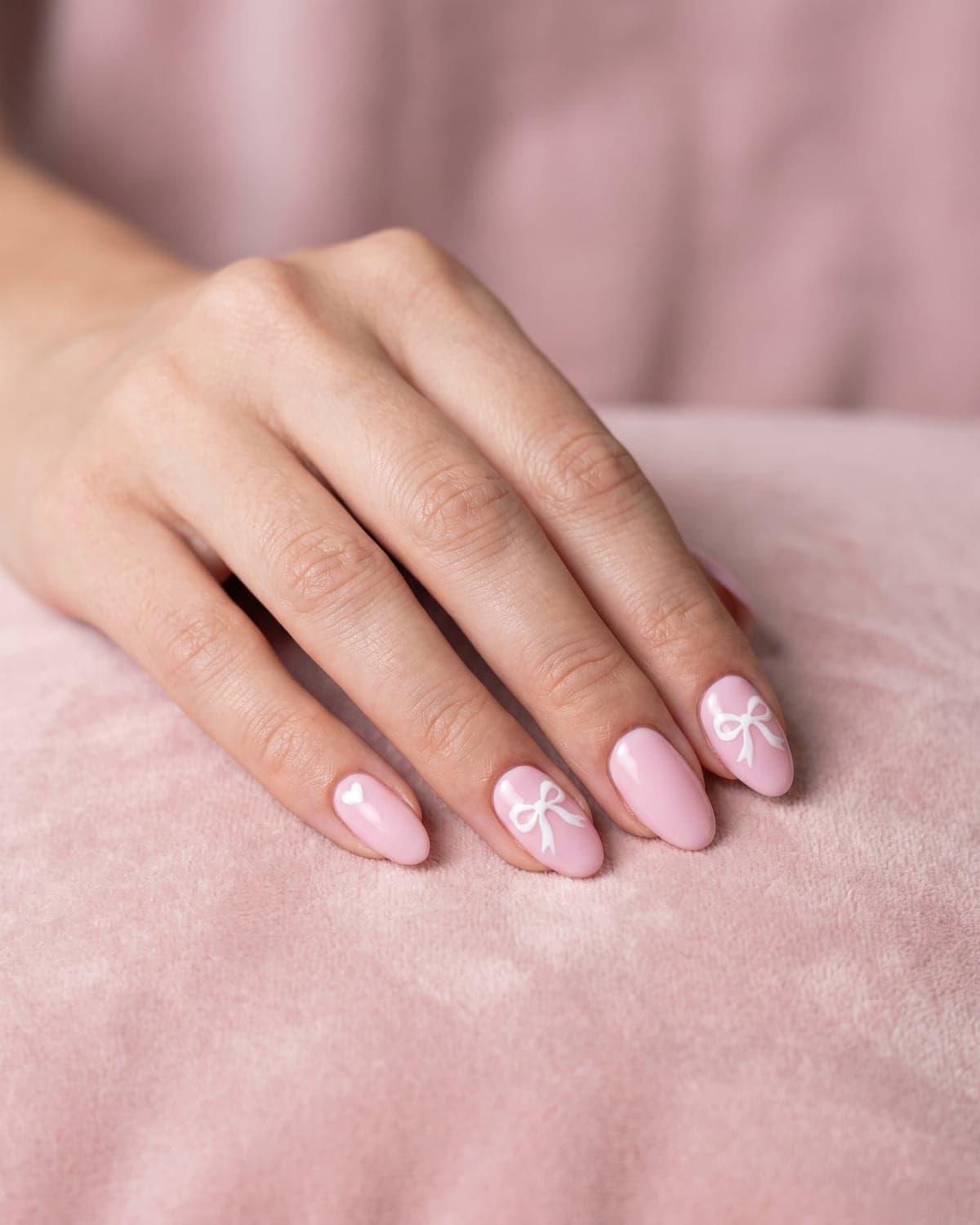 Pink oval nails with white bows and a heart accent nail on a soft pink background