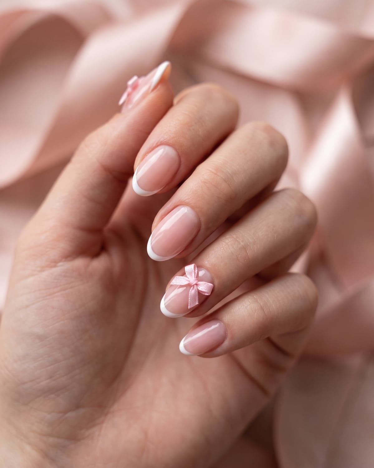 Pink micro French tip nails with pink and white bows on a blush background