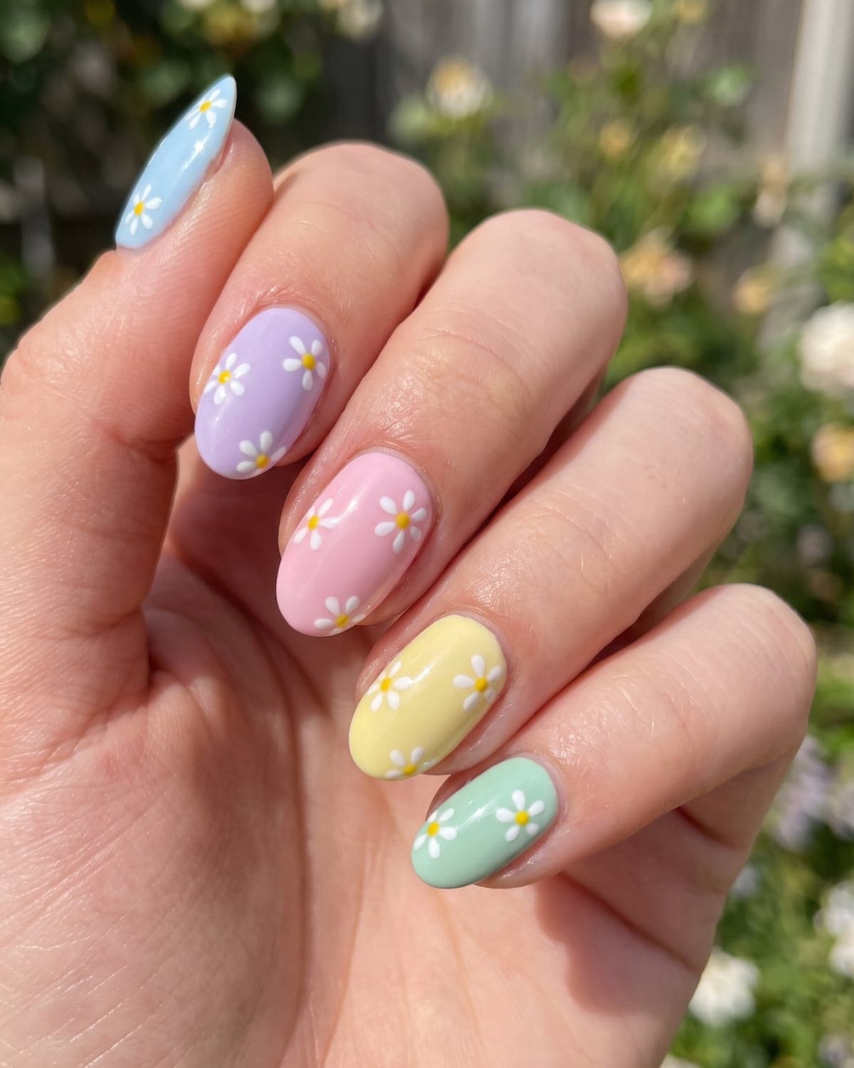 White daisy nail art on pastel blue, lilac, mint, yellow and pink nails