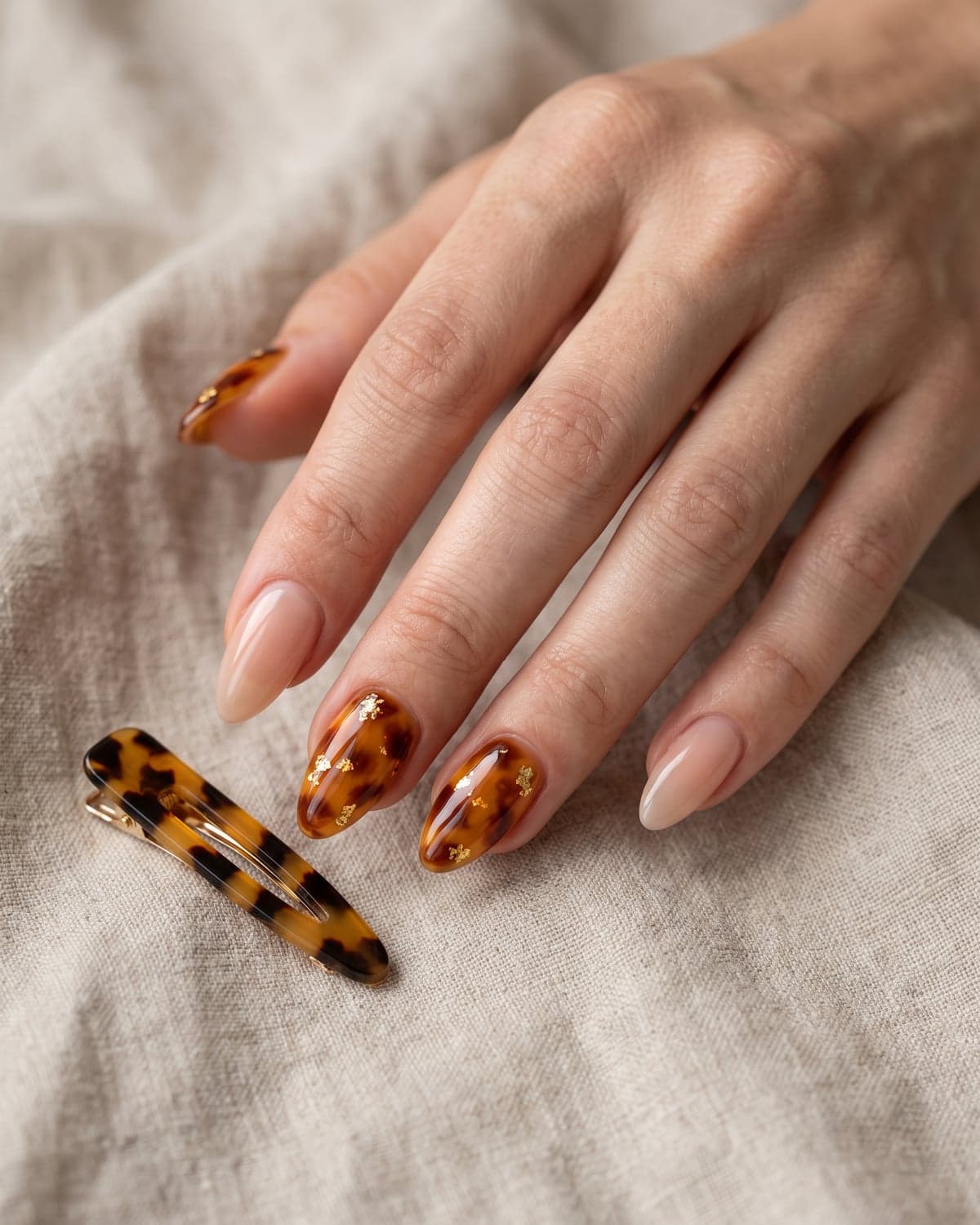Tortoiseshell and nude almond nails with gold foil on a warm beige background