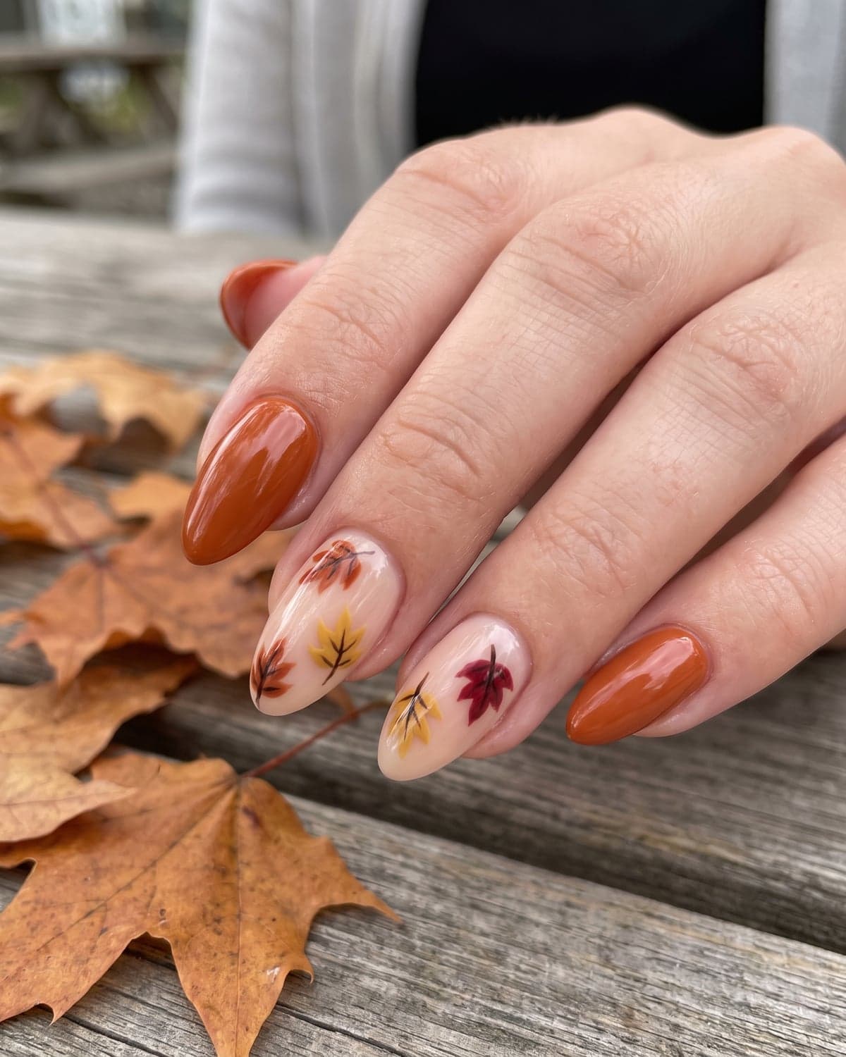 Fall leaf nail art in rust and mustard on nude almond nails, with solid burnt orange nails