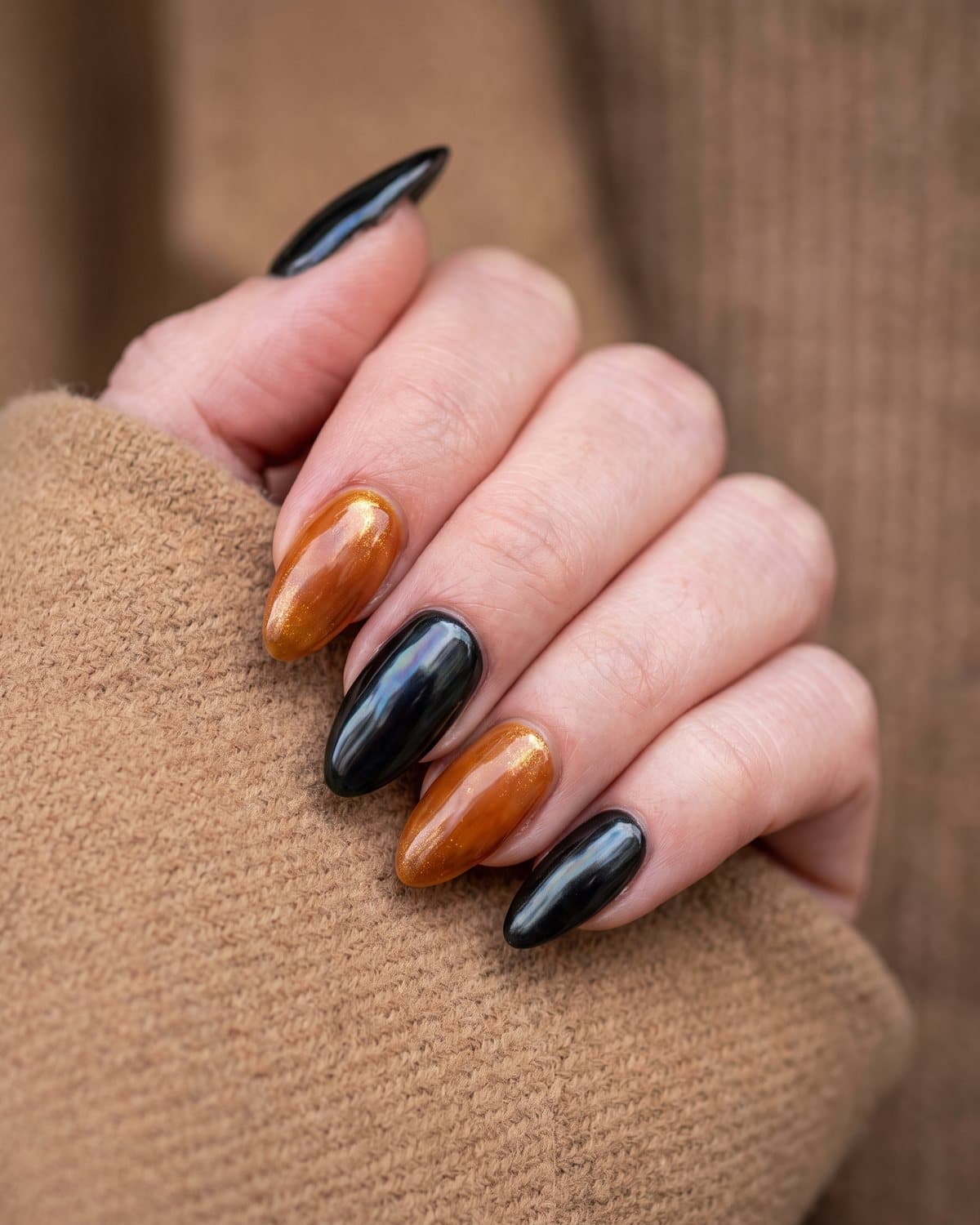 Almond nails alternating between iridescent black glazed and warm caramel honey glazed, on a camel wool coat