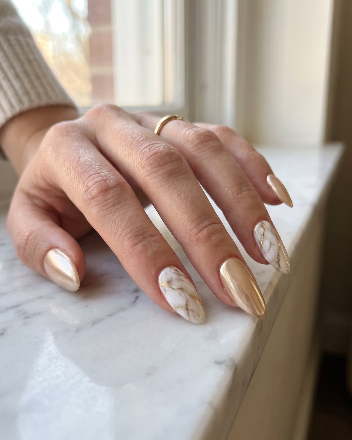 Almond nails with soft champagne gold glazed chrome and white marble with thin gold veins, on white marble