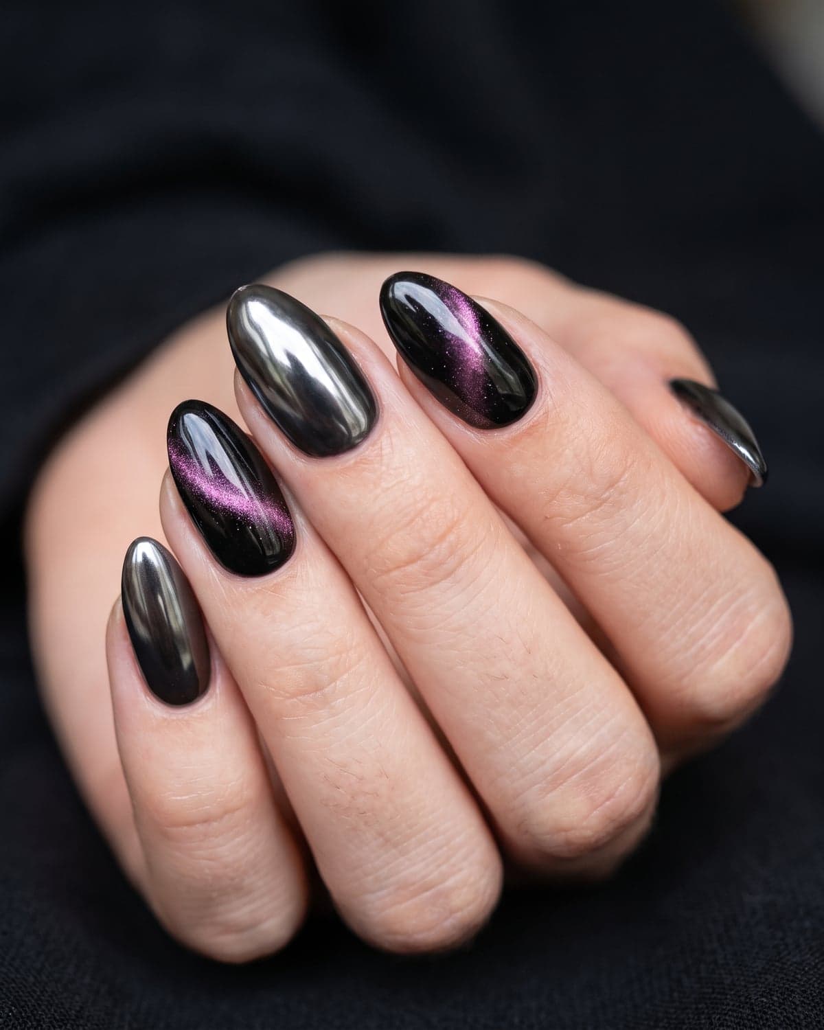 Black chrome and cat-eye almond nails with purple and pink shimmer on a dark background