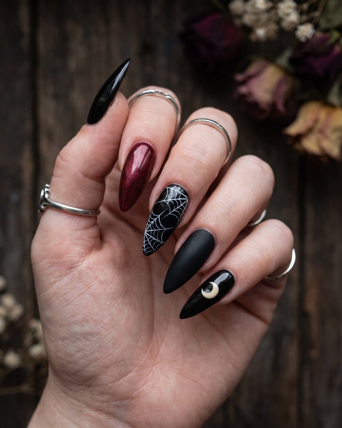 Gothic nail set with glossy black, oxblood velvet, spider web, matte black and moon designs on stiletto nails