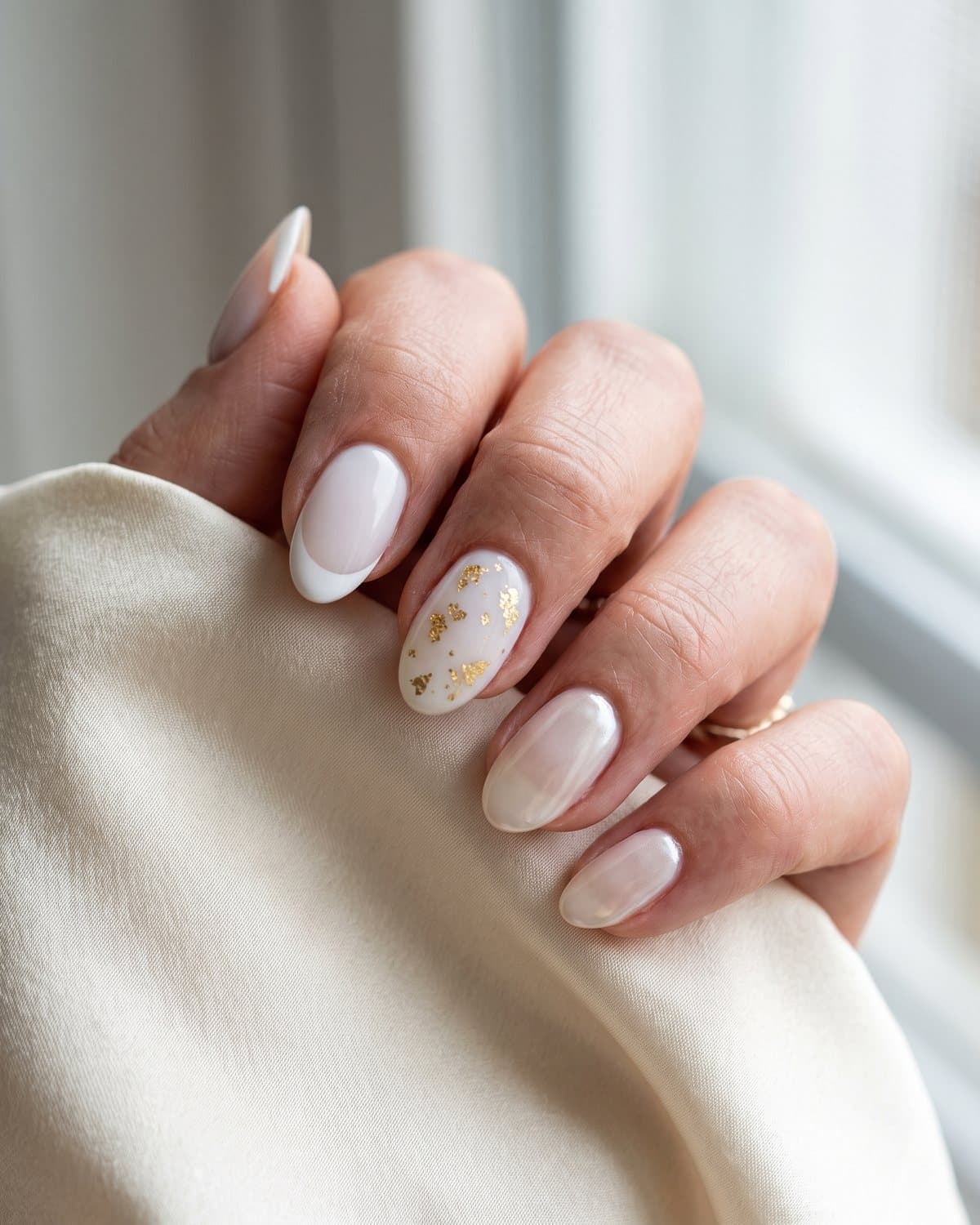 Oval nails with milky white and crisp white French tips, milky white with tiny gold flakes and milky white with a soft pearl glaze, on cream silk