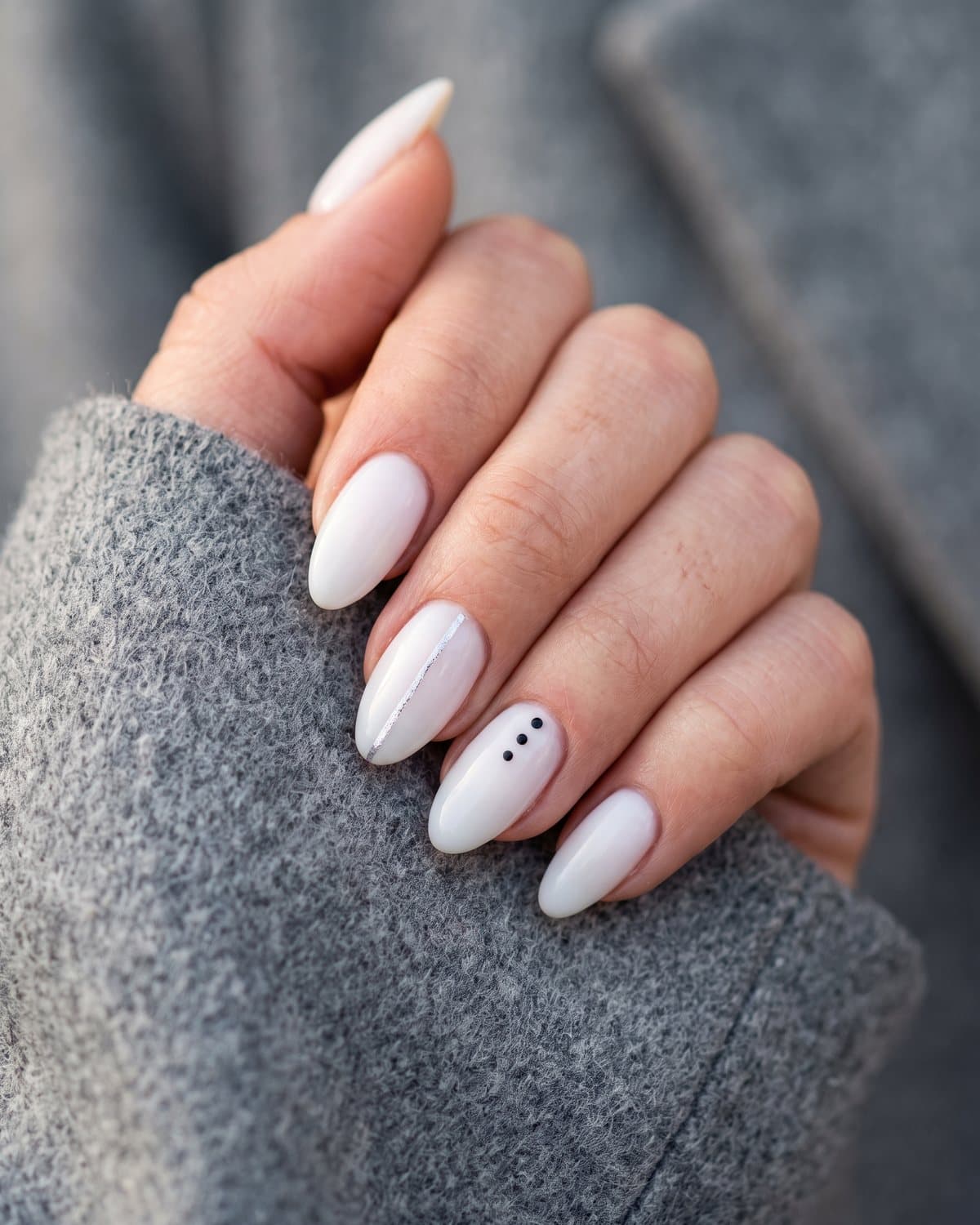 Almond nails with milky white and a fine vertical silver line, and milky white with three tiny black minimalist dots, on a grey wool coat