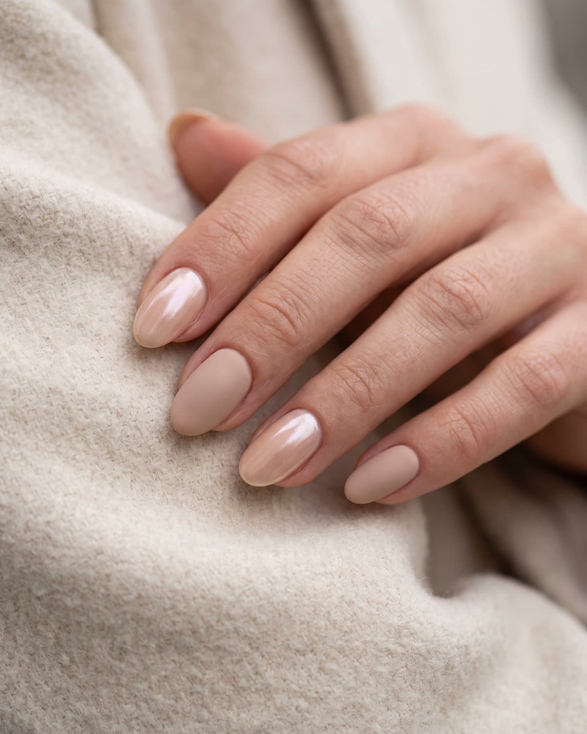 Oval nails with velvety matte beige nude alternating with glossy pearl chrome nude, on a cream wool coat