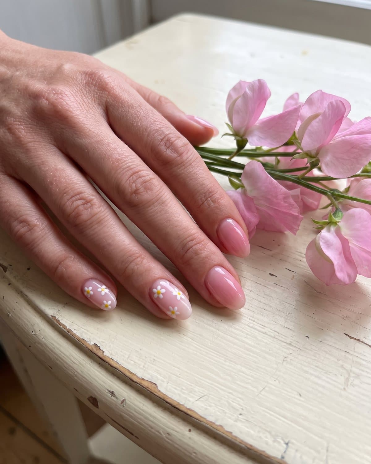 Oval nails in milky pink with tiny white flowers and translucent pink jelly nails, next to pink sweet peas