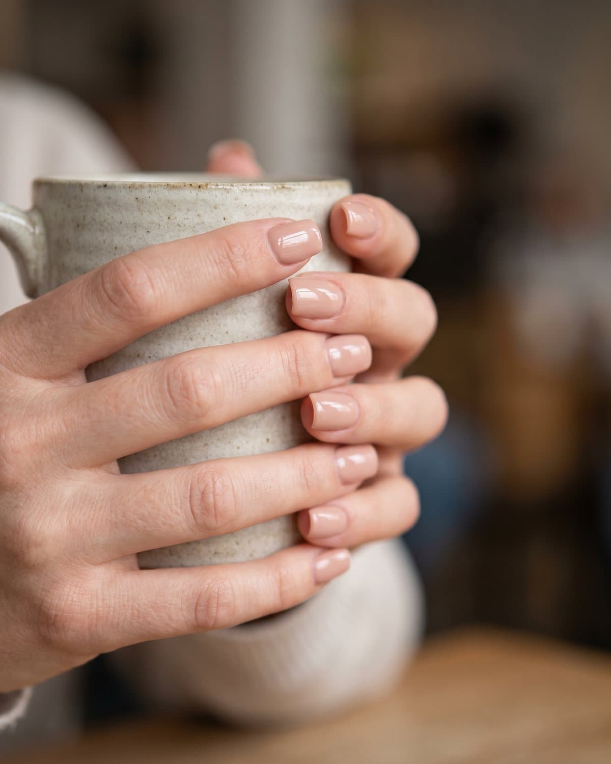 Short square acrylic nails in a glossy natural nude, clean and even, holding a ceramic cup