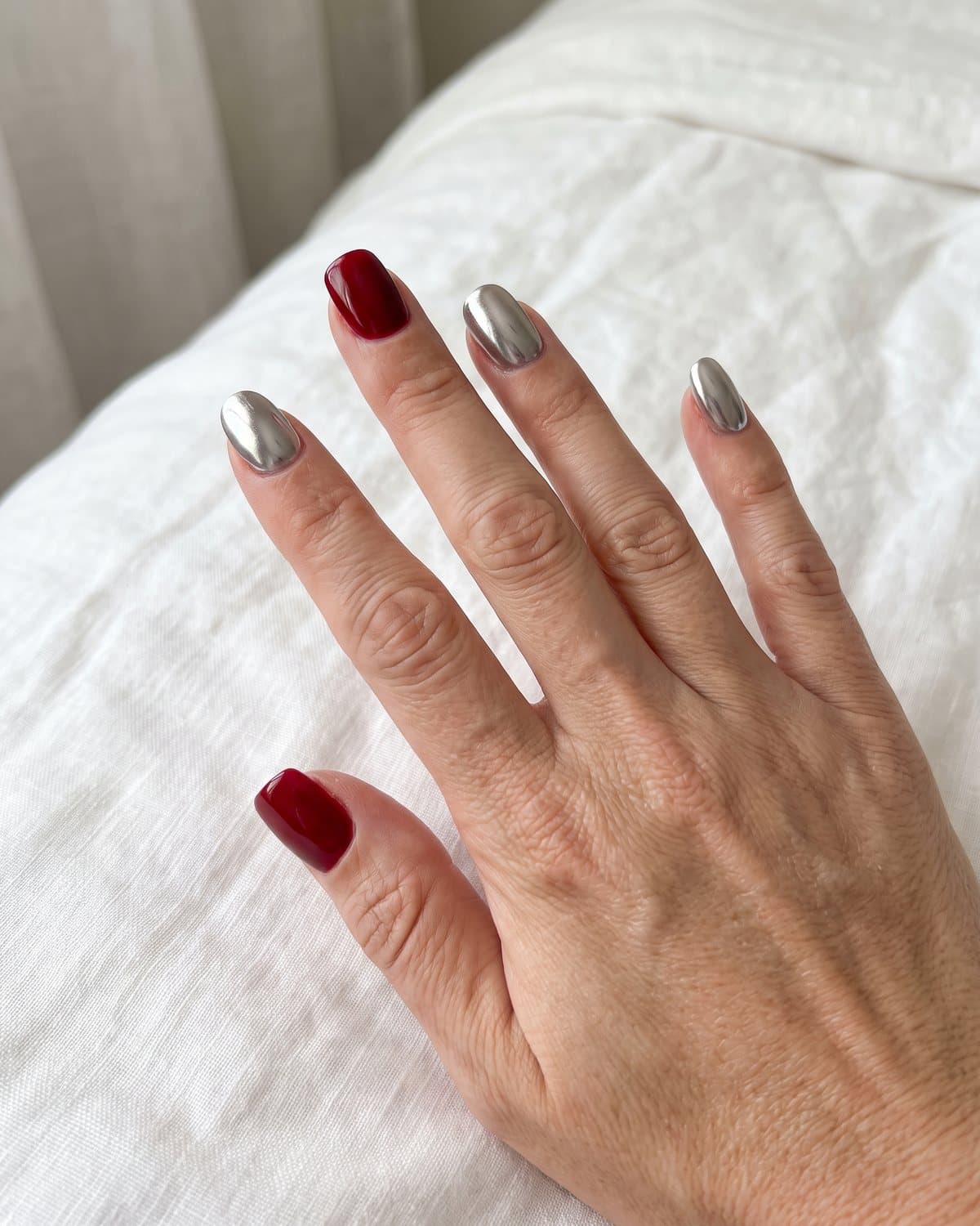 Short acrylic nails in glossy classic red square and short almond metallic silver chrome, on white linen