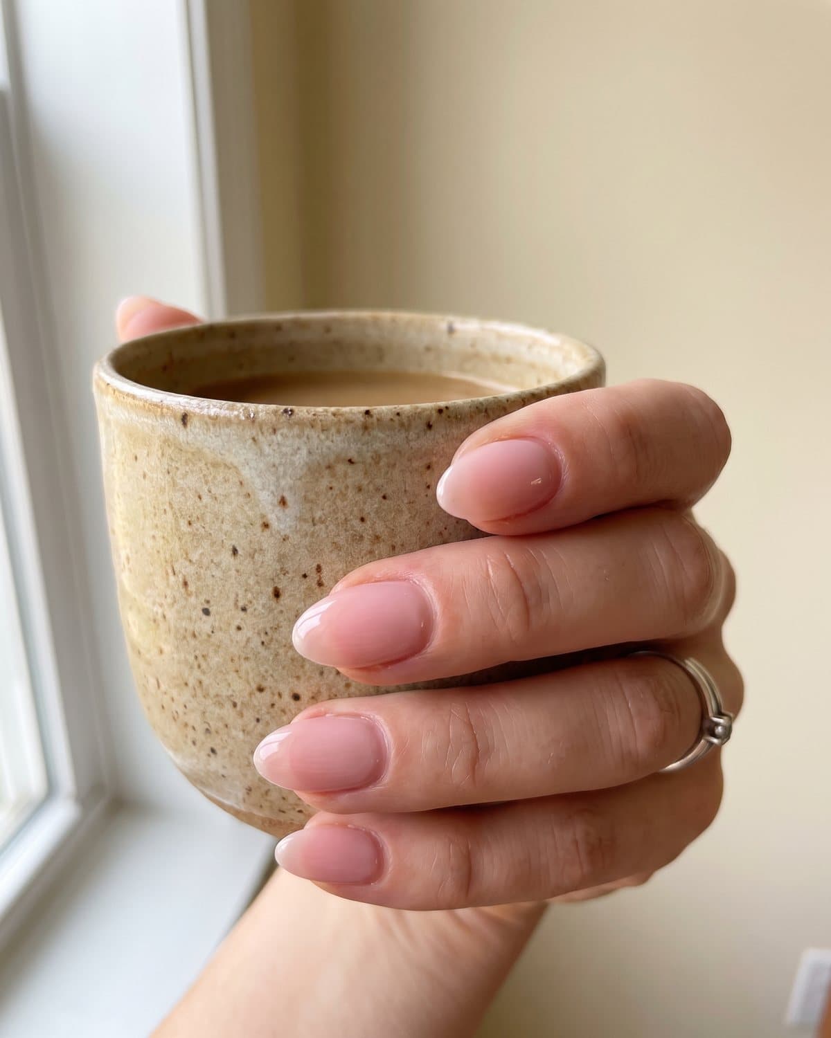 Short almond nails in a glossy sheer soft pink, holding a ceramic coffee cup