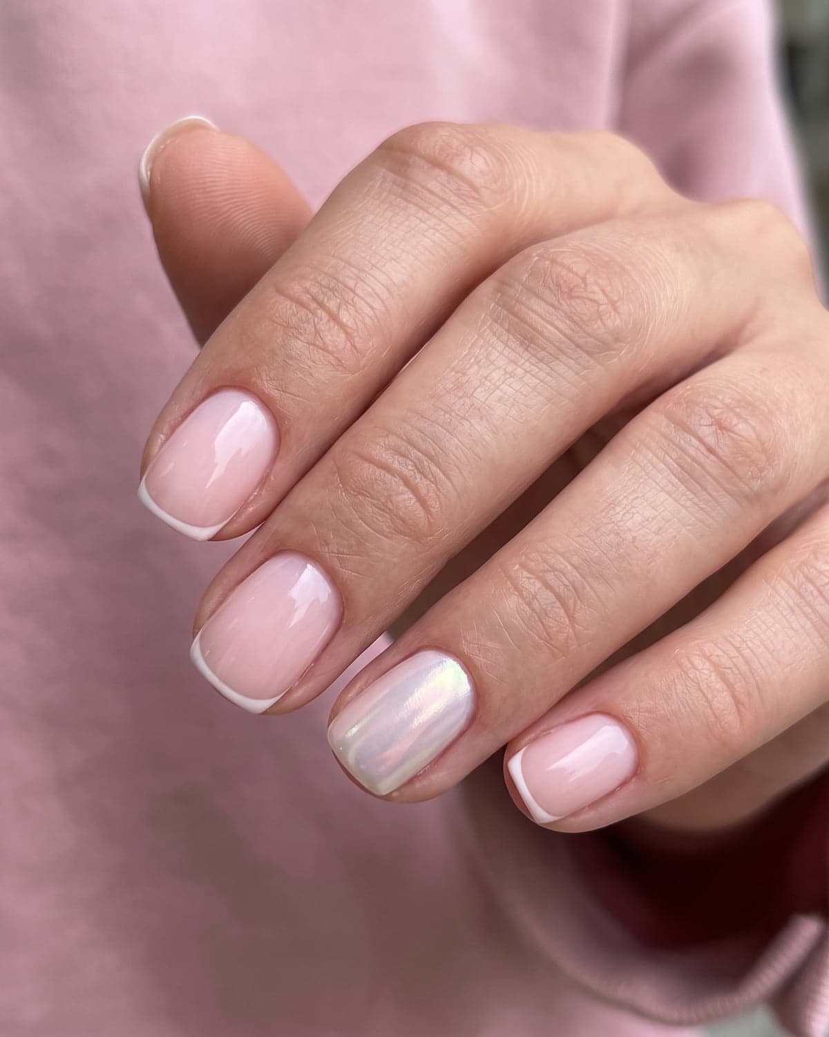 Milky pink short squoval nails with micro French tips and a glazed accent nail on a soft pink background