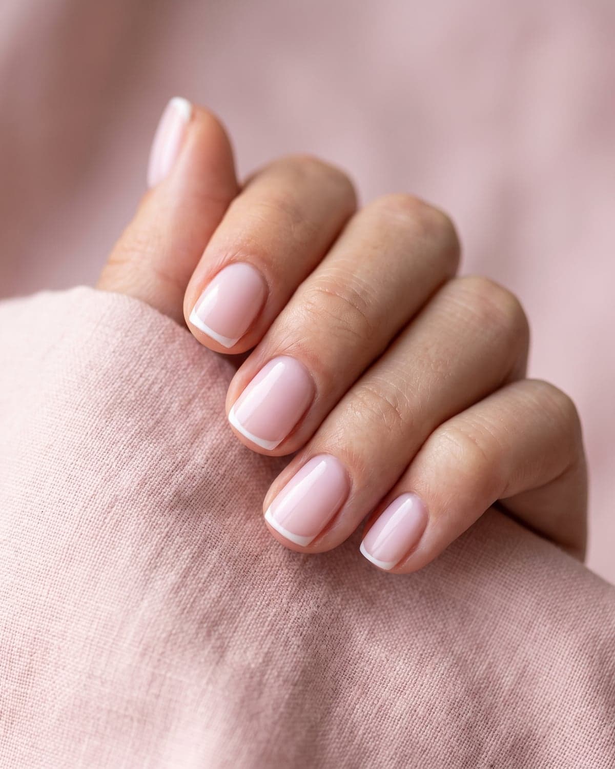 Milky pink short squoval nails with micro French tips on a soft pink background
