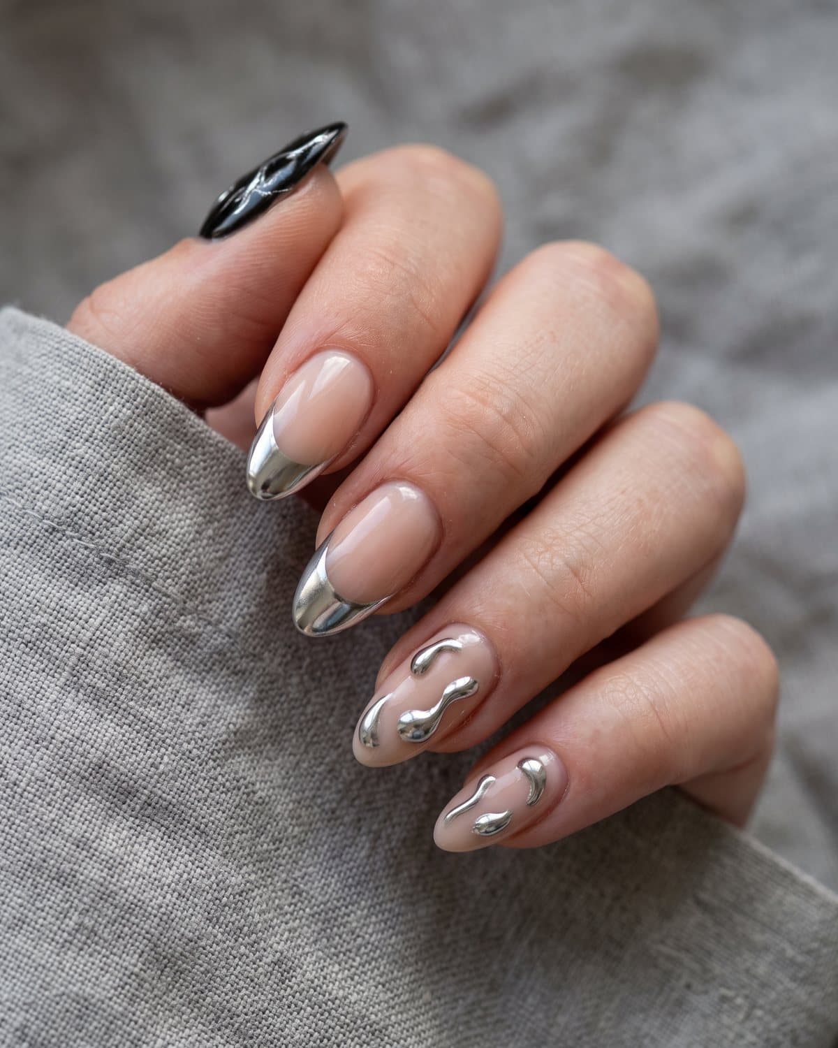 Almond nails with sheer nude and mirror silver chrome French tips, nude nails with 3D silver chrome droplets, and black nails with silver chrome accents