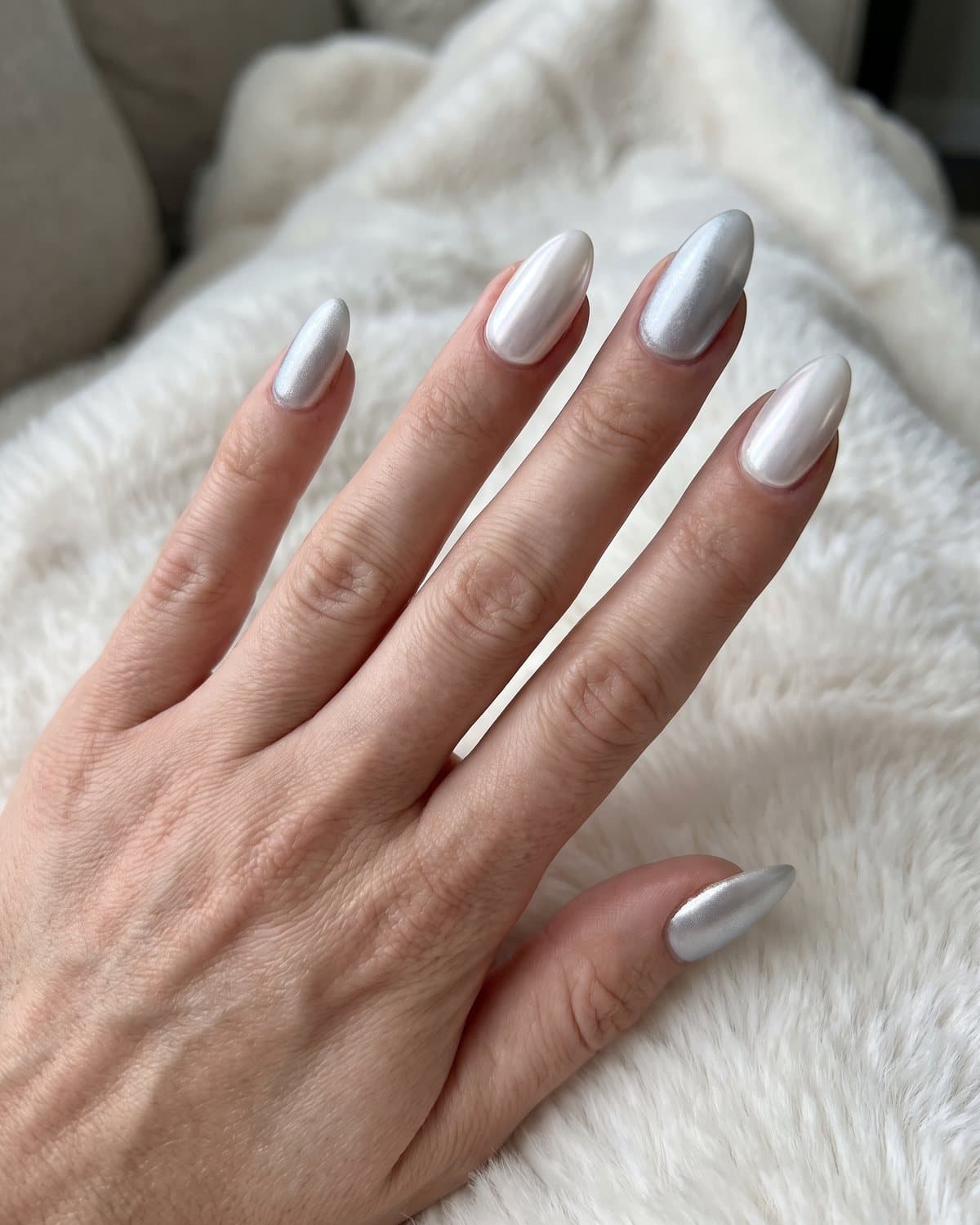 Almond nails with icy frosted silver chrome alternating with white pearl chrome, on white faux fur
