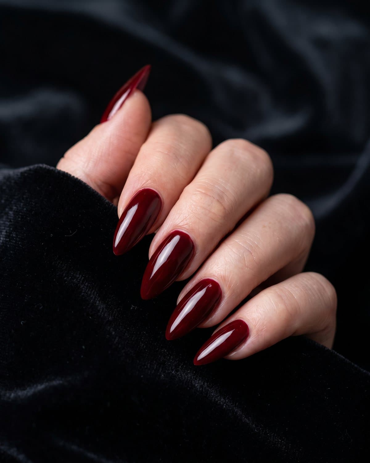 Long glossy stiletto nails in a rich blood red, resting on black velvet