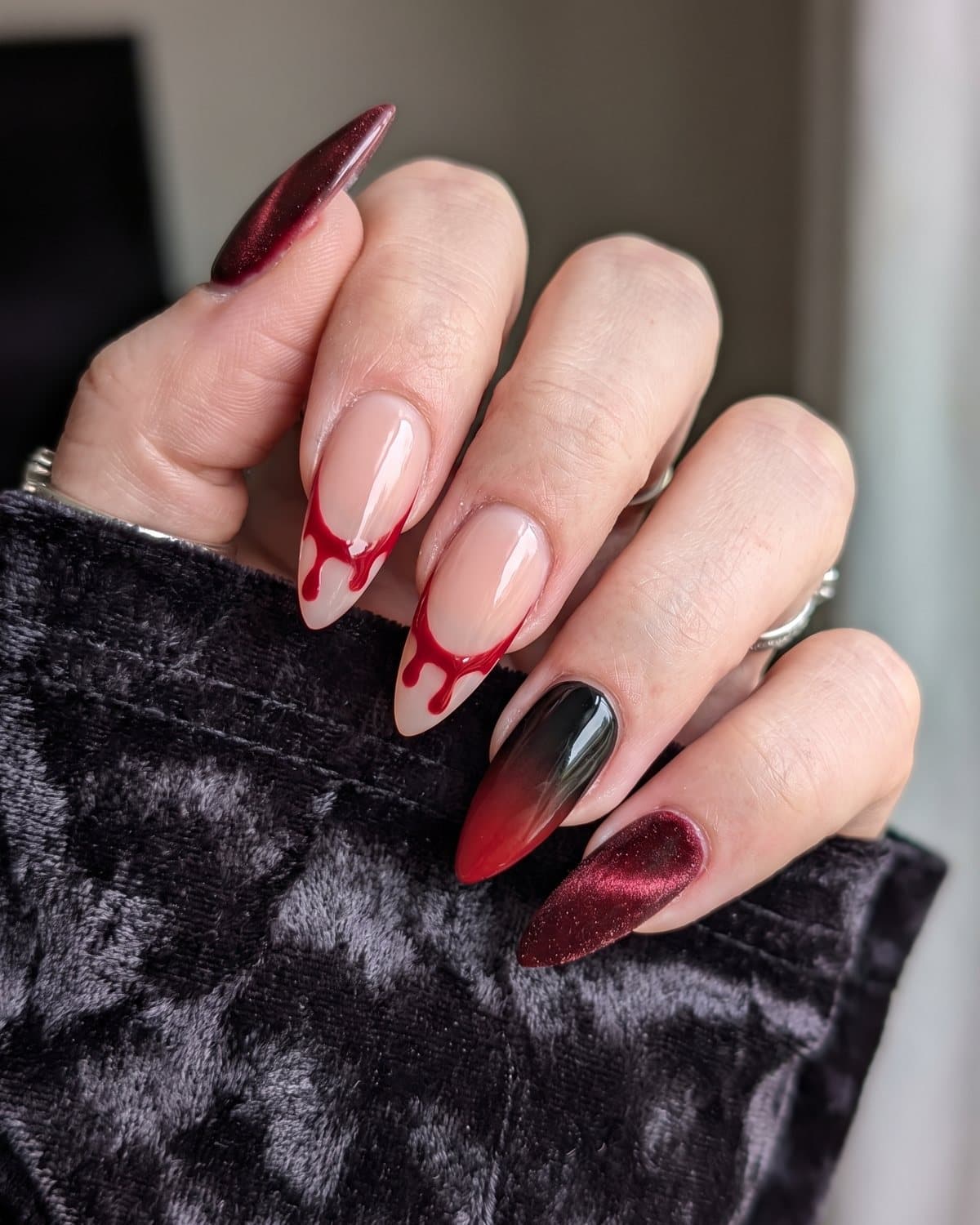 Stiletto nails with oxblood velvet cat-eye, sheer nude nails with red blood-drip French tips and black to red ombré, on dark velvet