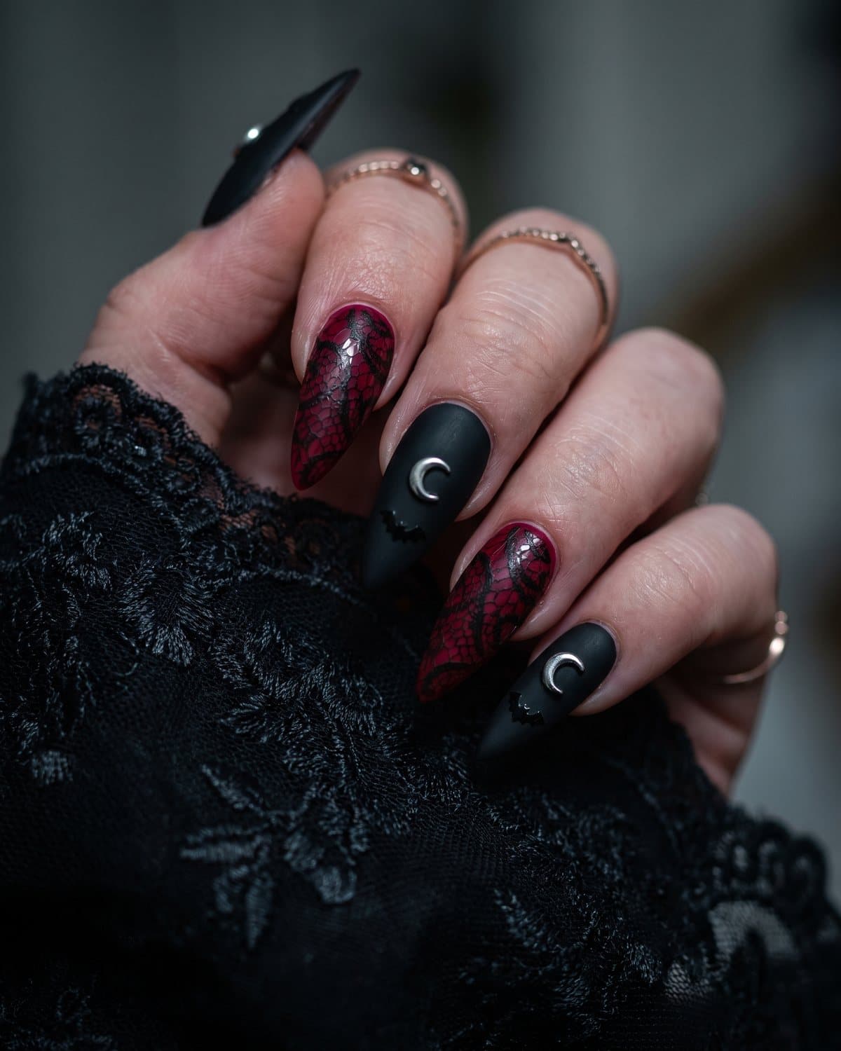 Stiletto nails in deep red with black lace overlay and black nails with a silver crescent moon and a tiny bat, on black lace
