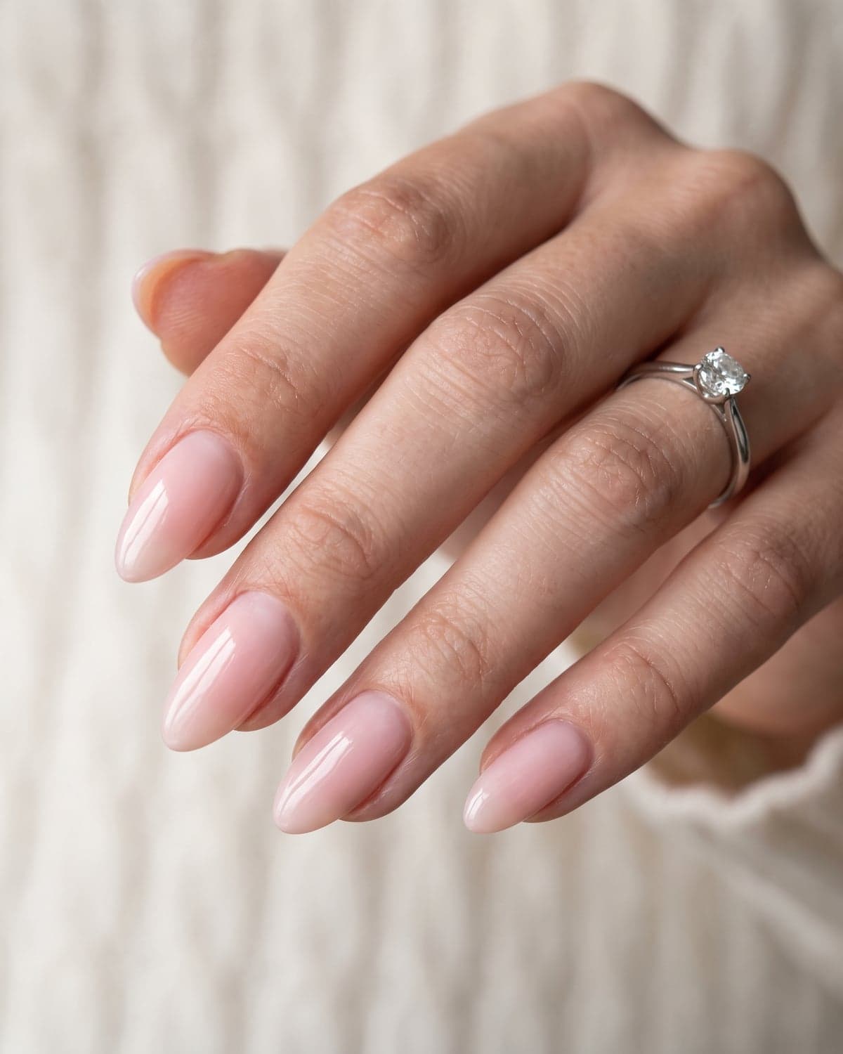 Sheer bridal pink almond nails with a glossy finish on a soft ivory background