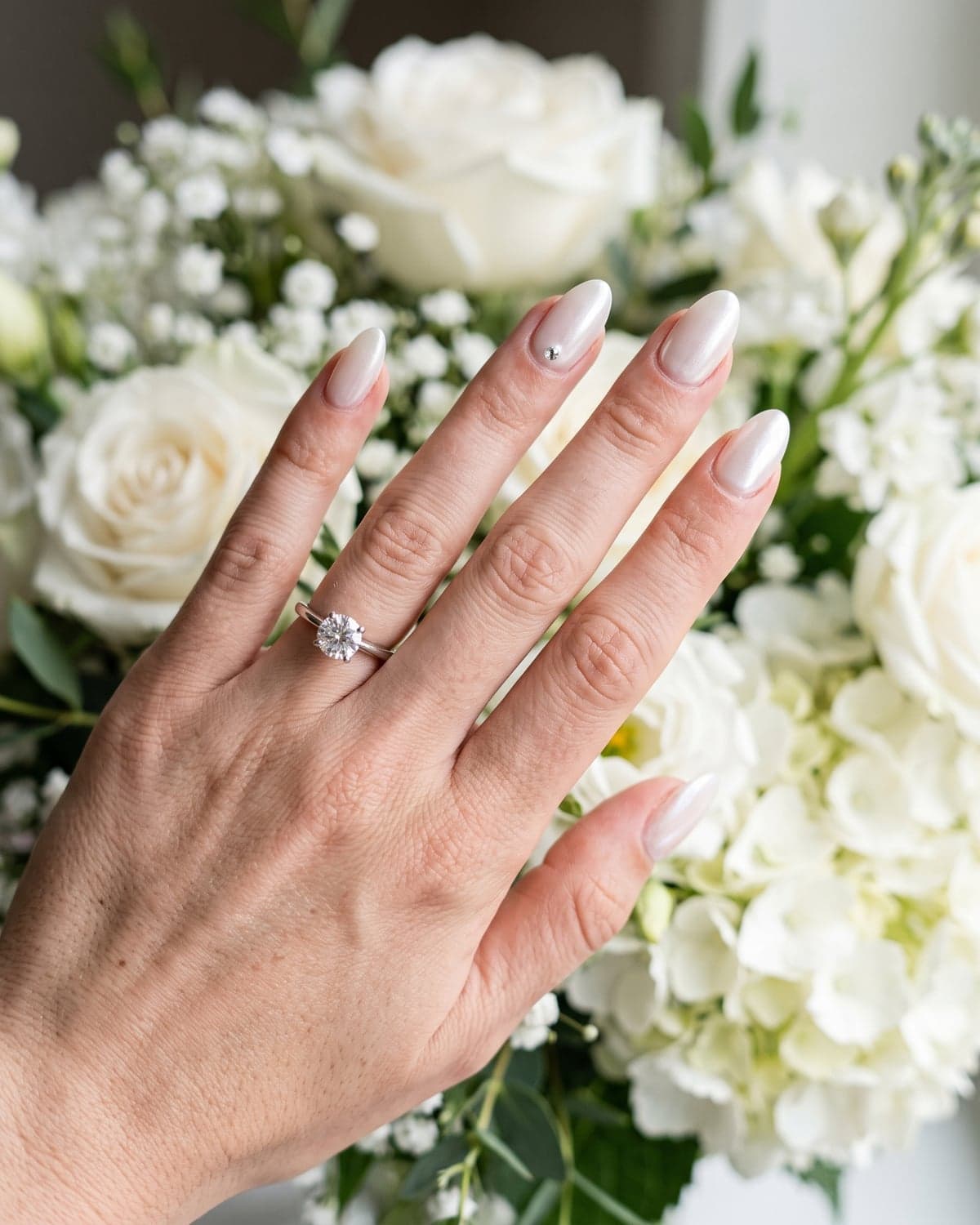 White glazed bridal almond nails with a pearly finish and a crystal accent
