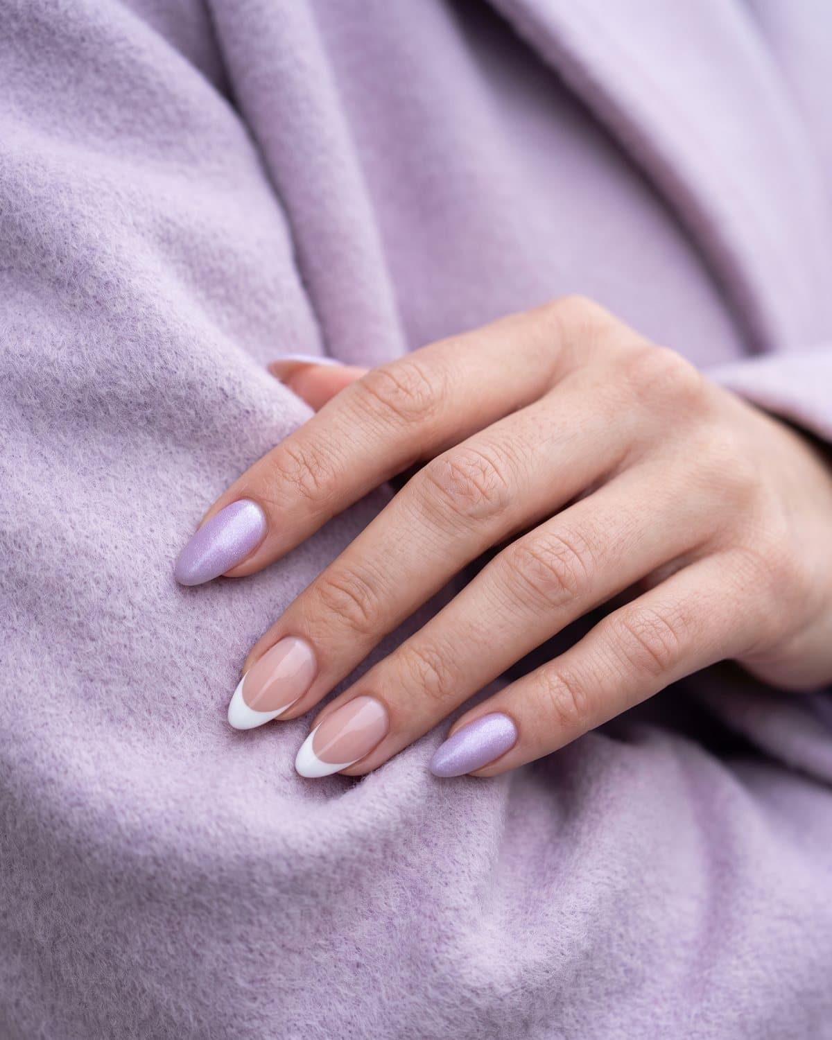 Almond nails with frosted lilac shimmer and sheer nude with crisp white French tips, on a pale lilac wool coat