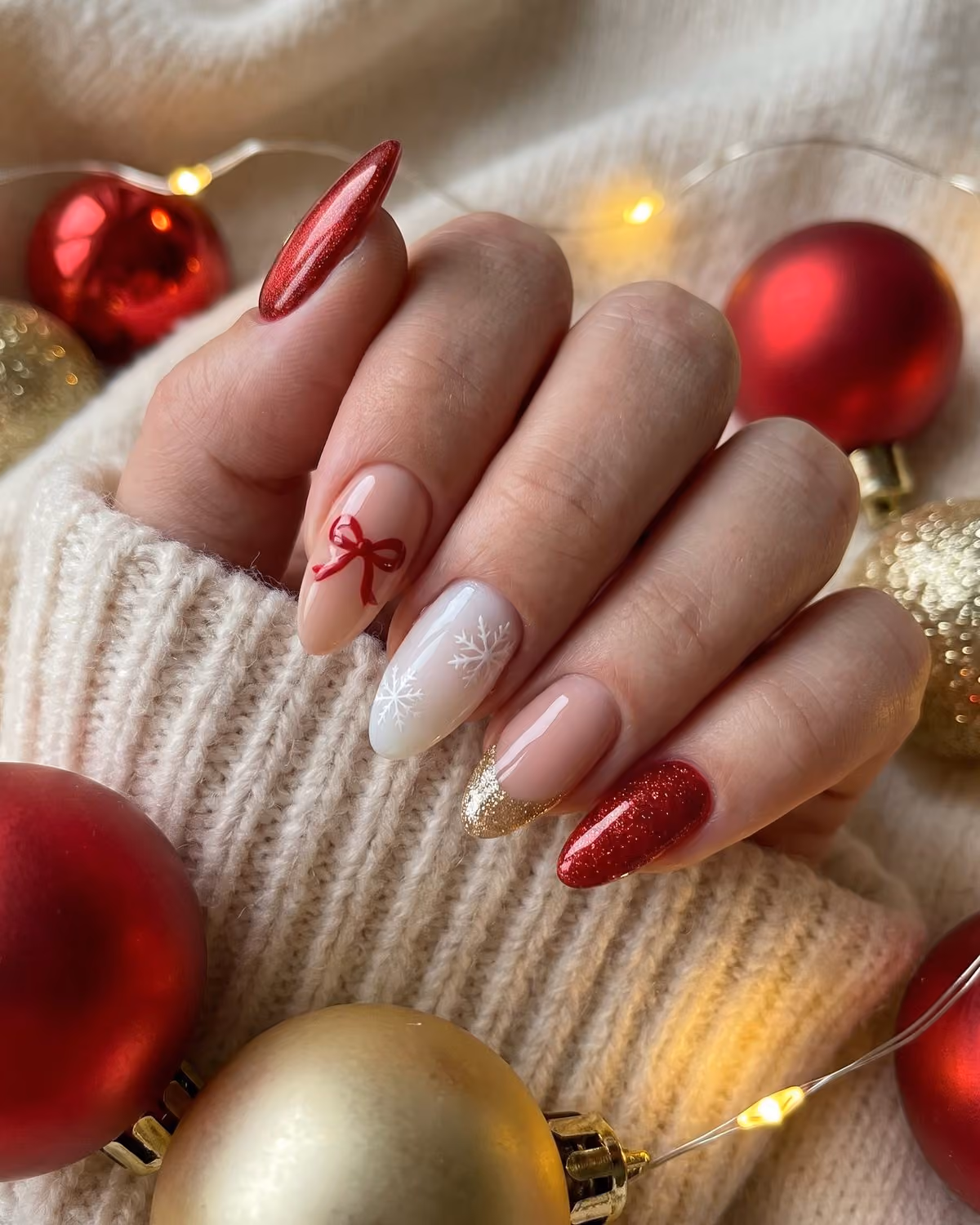 Almond Christmas nails with red velvet cat-eye, a tiny red bow, a white snowflake and gold glitter French tip among red and gold ornaments