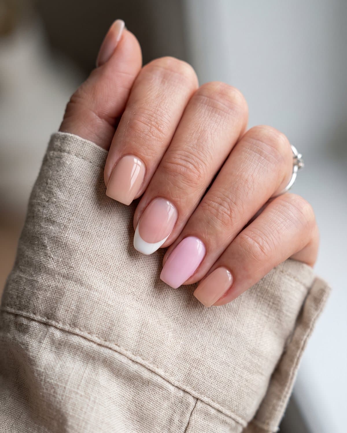 Short natural-looking acrylic nails in square nude, soft pink coffin and almond white French tips, on a beige linen shirt